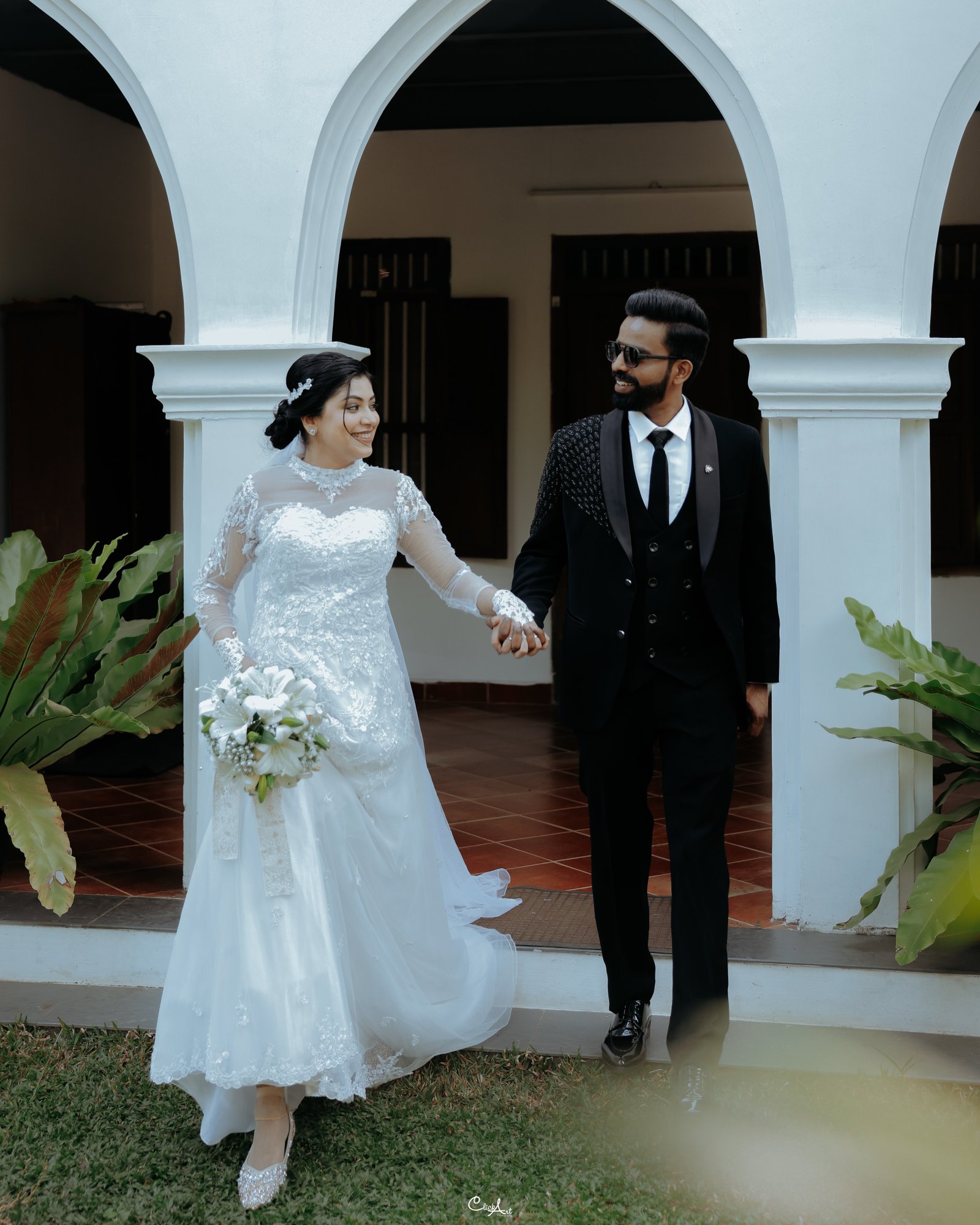 A bride and groom walking together beneath white arches